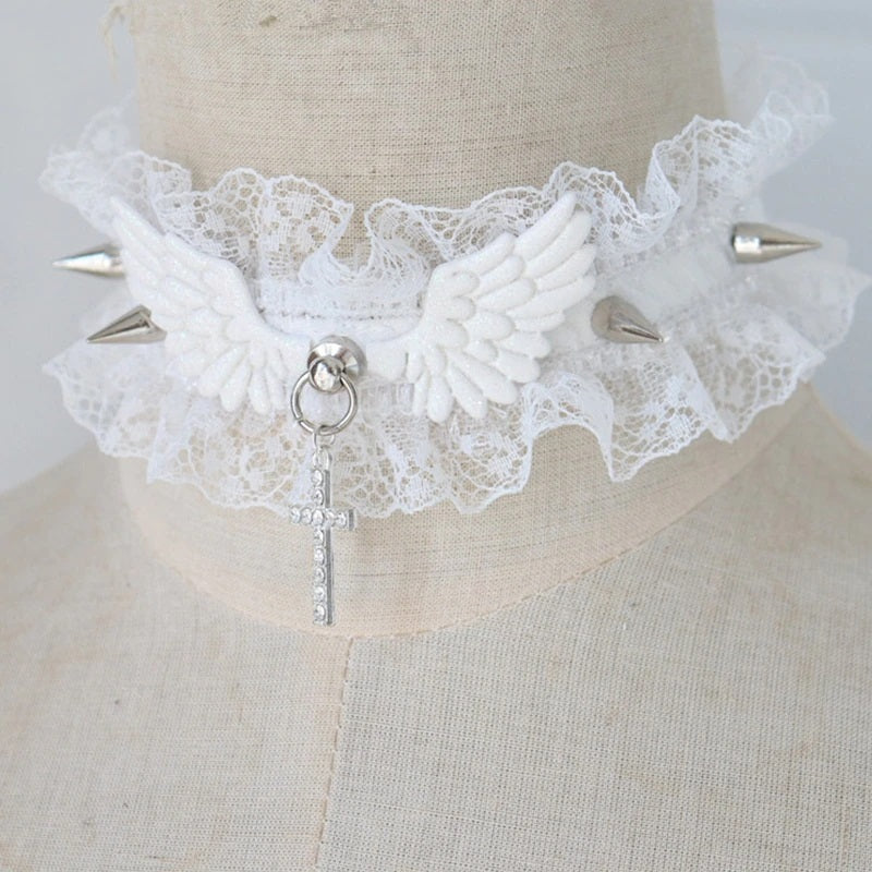 Product shot of a white pastel goth ruffled lace choker featuring white angel wings, silver metal spikes, a rhinestone cross pendant, and an adjustable silver clasp.