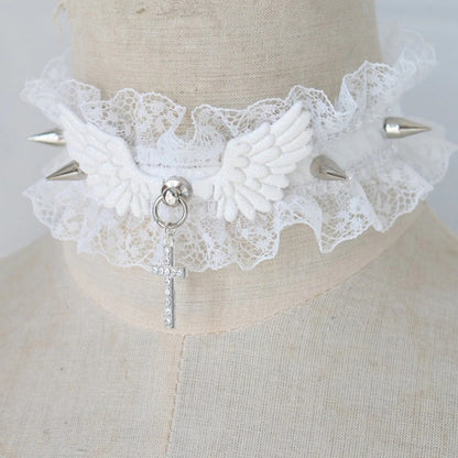 Product shot of a white pastel goth ruffled lace choker featuring white angel wings, silver metal spikes, a rhinestone cross pendant, and an adjustable silver clasp.