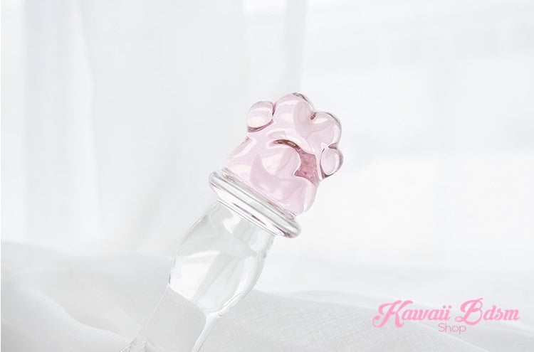 Clear borosilicate glass pleasure wand with a pink paw handle resting elegantly on soft white silk fabric.