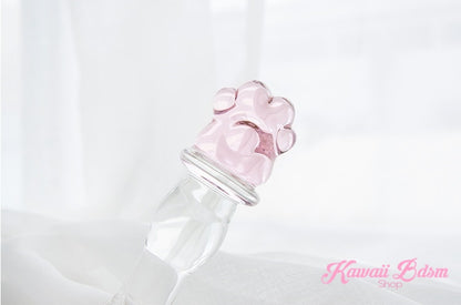Clear borosilicate glass pleasure wand with a pink paw handle resting elegantly on soft white silk fabric.