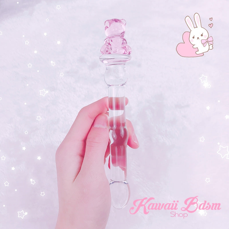 Hand holding the slim pink teddy bear BDSM wand against a sparkling pastel pink background with a cute bunny illustration.