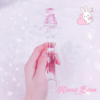 Hand holding the slim pink teddy bear BDSM wand against a sparkling pastel pink background with a cute bunny illustration.