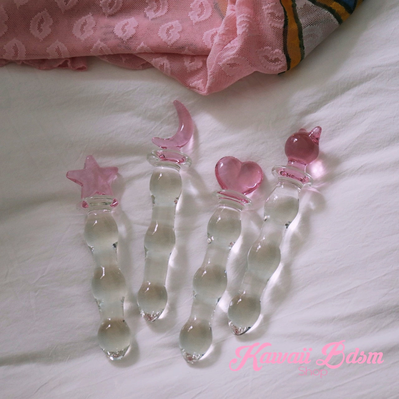 A collection of cute pink kitty handle glass pleasure wands resting playfully on a soft bed with white and pink sheets.