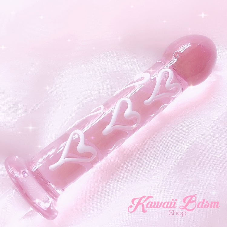 Close-up of the pastel pink glass dildo with white hearts resting elegantly on soft pink fabric.