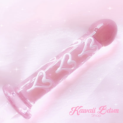 Close-up of the pastel pink glass dildo with white hearts resting elegantly on soft pink fabric.
