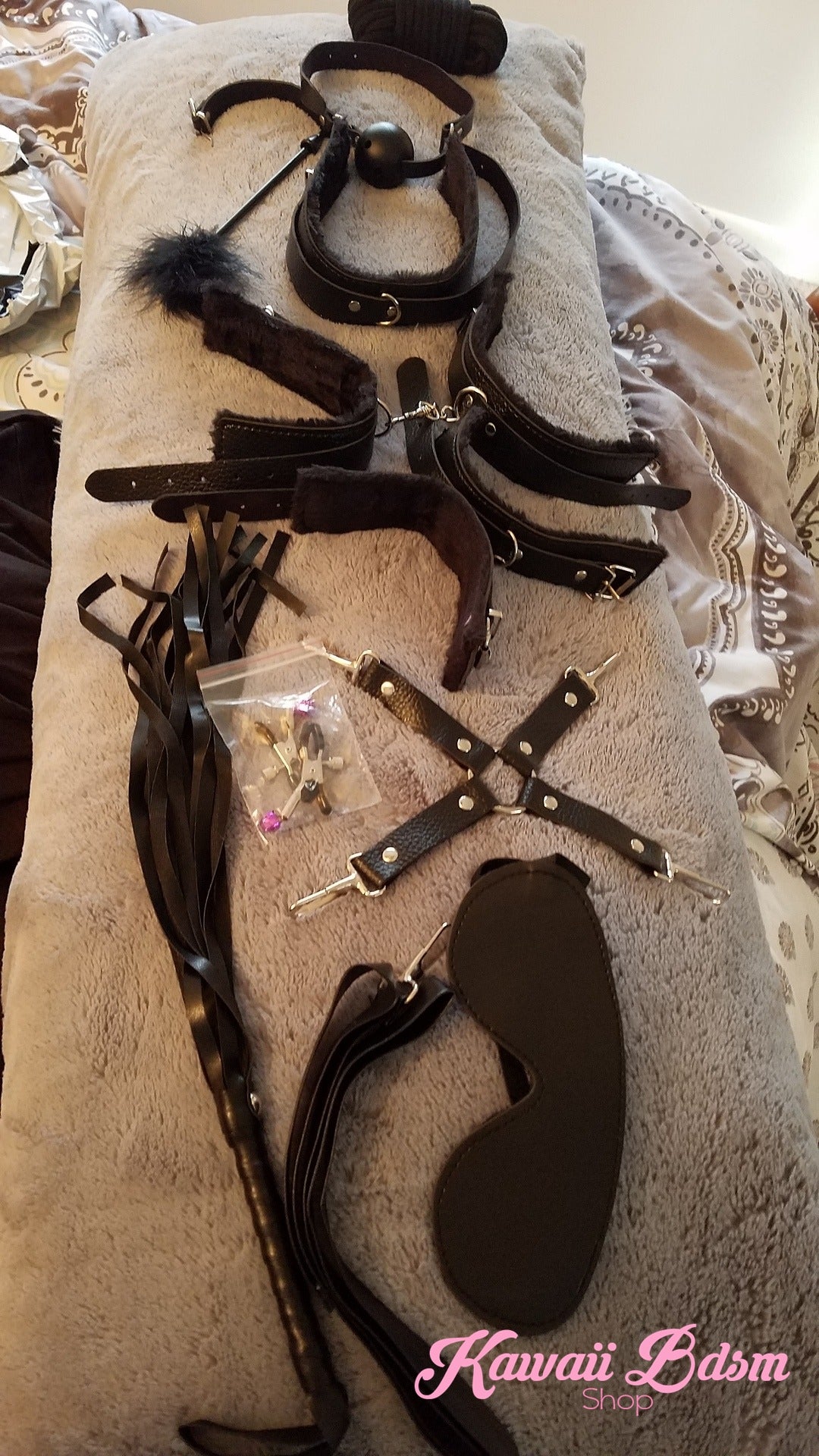 Real product view of the 10-piece black bondage set on a textured background showing the soft plush materials.