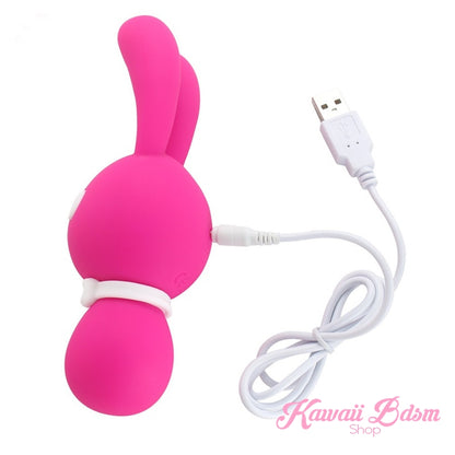 A solid hot pink Mitzi bunny vibrator shown from the side with its white USB charging cable plugged in.