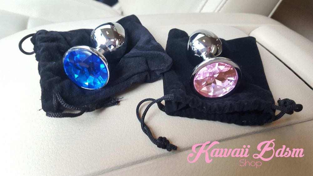 Two beautiful stainless steel jewel plugs, one blue and one pink, resting elegantly on top of black velvet storage pouches.
