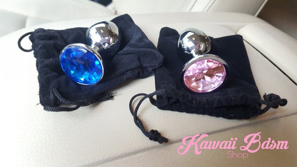 Two beautiful stainless steel jewel plugs, one blue and one pink, resting elegantly on top of black velvet storage pouches.