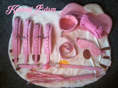 Kawaii BDSM kit displayed on a white fluffy rug, featuring the pink blindfold and ball gag.