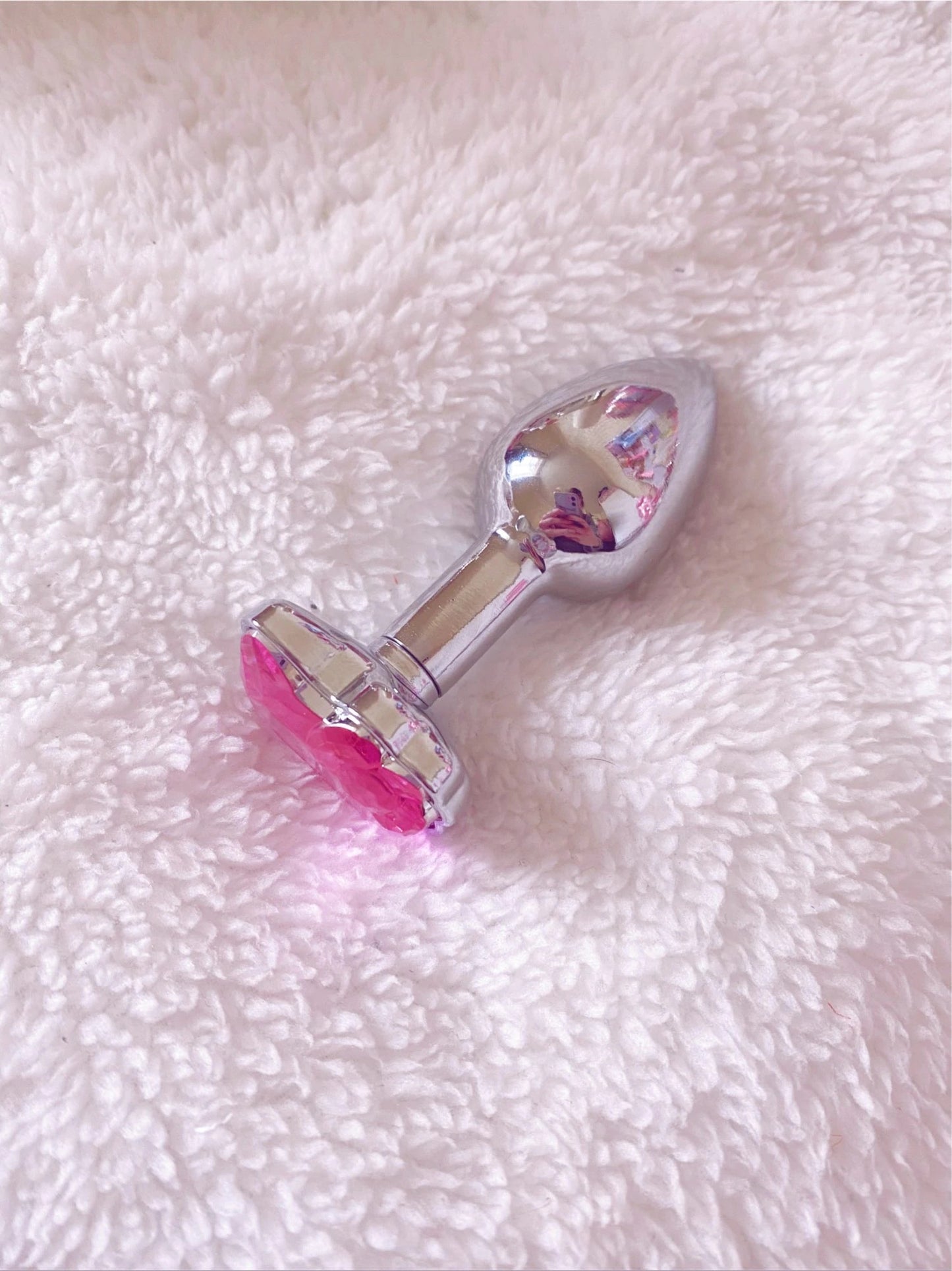 Cute stainless steel Hello Kitty anal plug laying on a soft white fluffy background, highlighting the pink gem and smooth metal finish.
