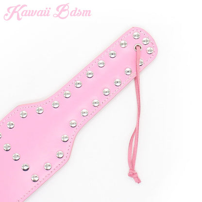 Angled view of the cute pink spanking paddle showcasing the shiny silver studs and the attached security wrist strap.