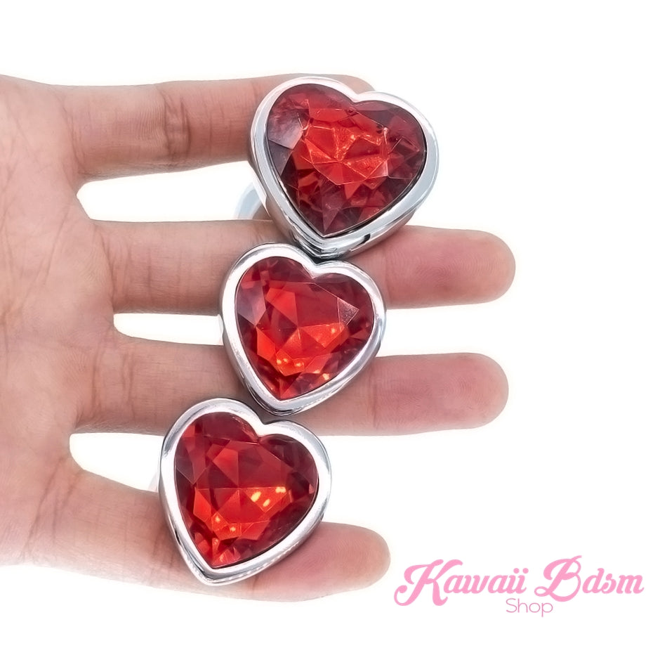 A hand displaying a beautiful 3-piece ruby red crystal heart stainless steel training plug set.