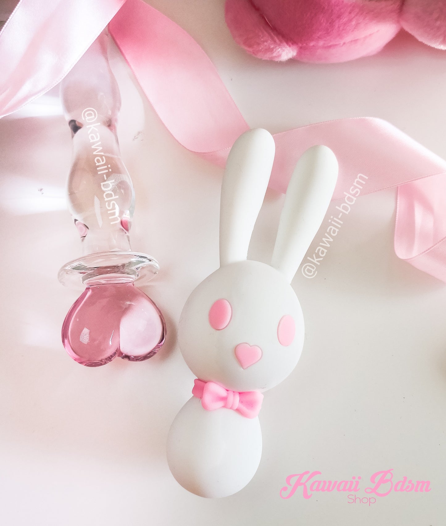 An aesthetic lifestyle photo of the white and pink Mitzi bunny vibrator resting on a soft surface with pink satin ribbons.